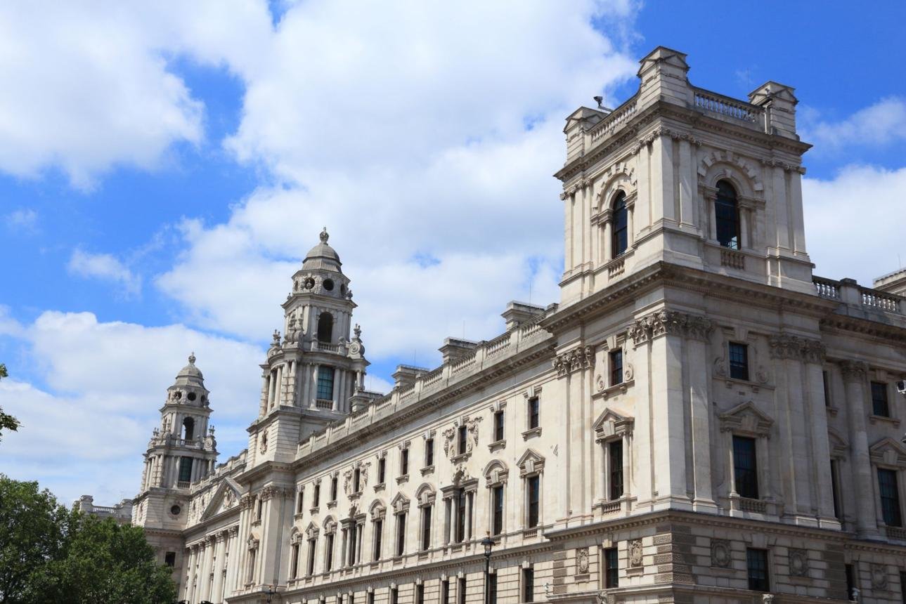 Neoclassical stone building with tall decorative towers under a blue sky; ornate windows and façades stretch along the street.
