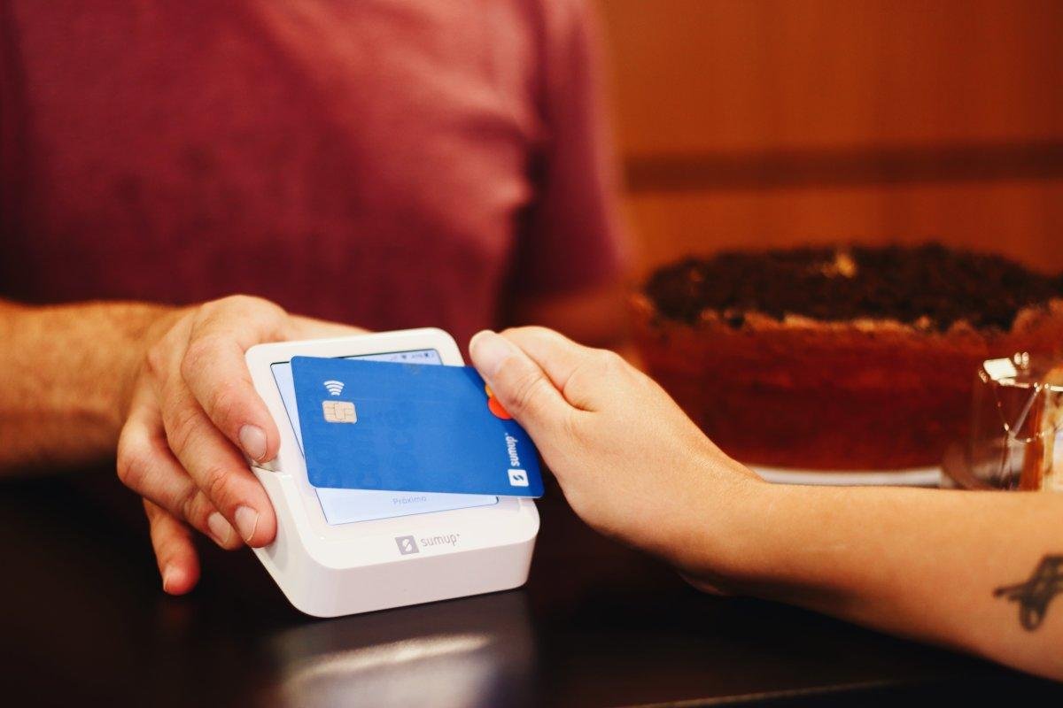 Person placing a blue contactless card on a white SumUp card reader to pay.